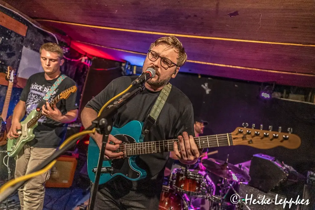 Andreas Gaida von Kip Kasper singt live im Wild Rover in Aachen ins Mikrofon, während die Band im Hintergrund spielt.