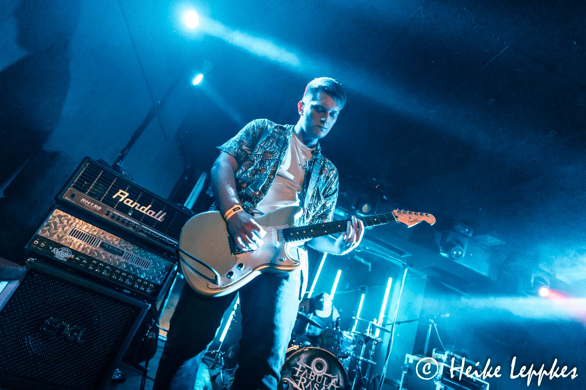 Rafael Gebhardt von Kip Kasper spielt live im MTC Köln E-Gitarre auf der Bühne – mit Verstärker und Mikrofon während das Bühnenlicht seinen Schatten wirft.
