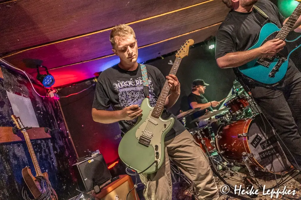 Rafael Gebhardt von Kip Kasper spielt live im Wild Rover Aachen E-Gitarre auf der Bühne – mit Verstärker und Mikrofon während das Bühnenlicht seinen Schatten wirft.